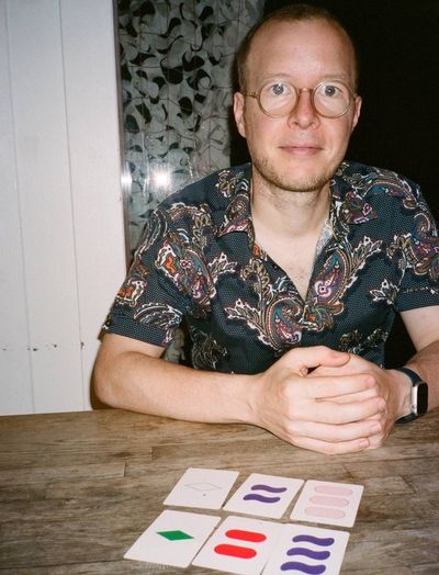 Rob Knight, sat at a table with a game of Set laid out